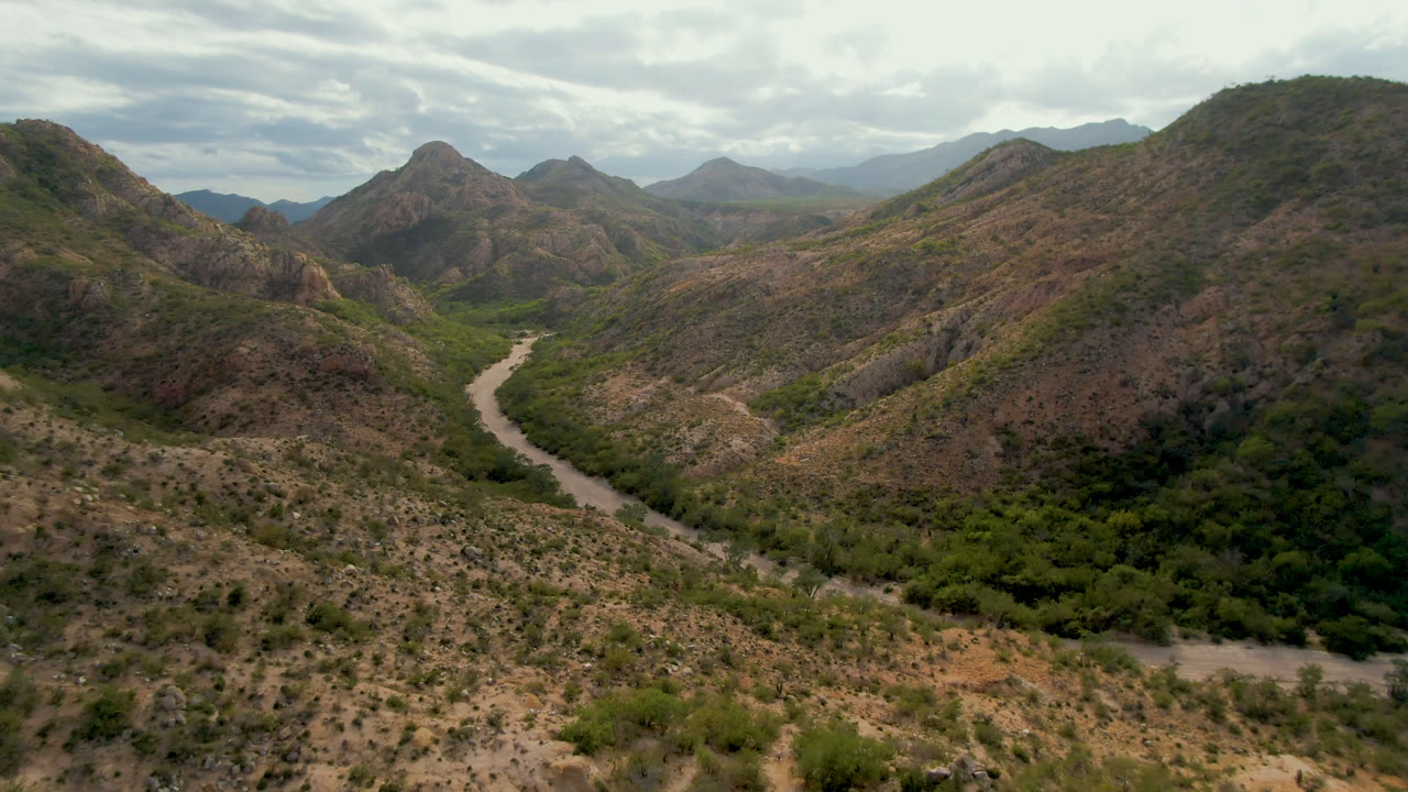 Wide aerial landscape with dry mountain slopes, green valley, and distant ridges