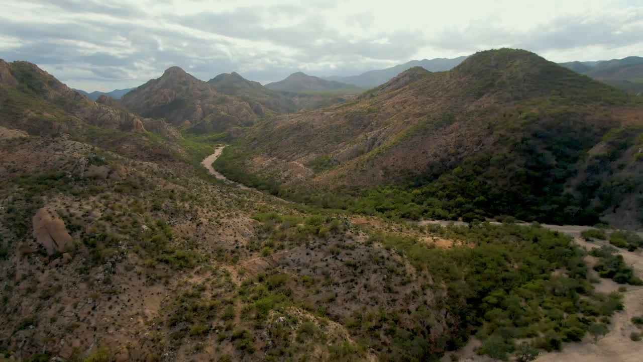 Aerial landscape of rugged hills and a winding road below clouds.