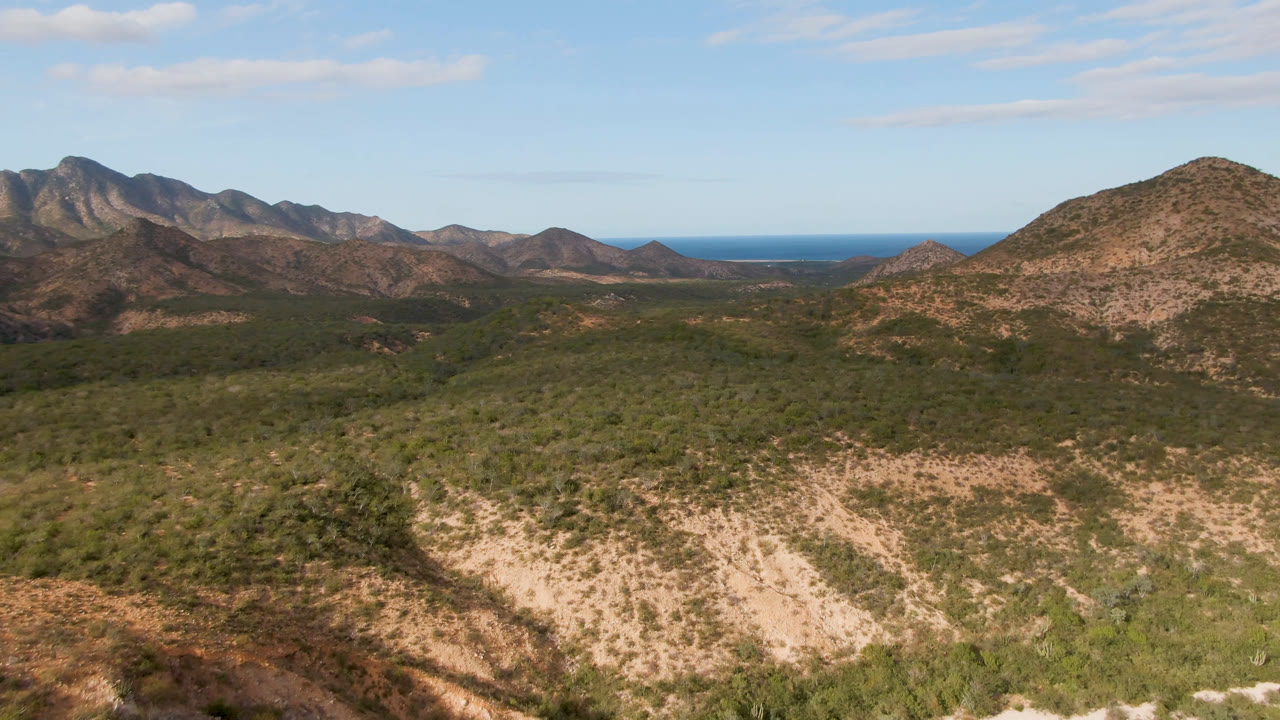 Cabo Pulmo, Baja California Sur view looking over a tan rocky ridge and green desert vegetation toward layered mountains and distant water, with no visible people.
