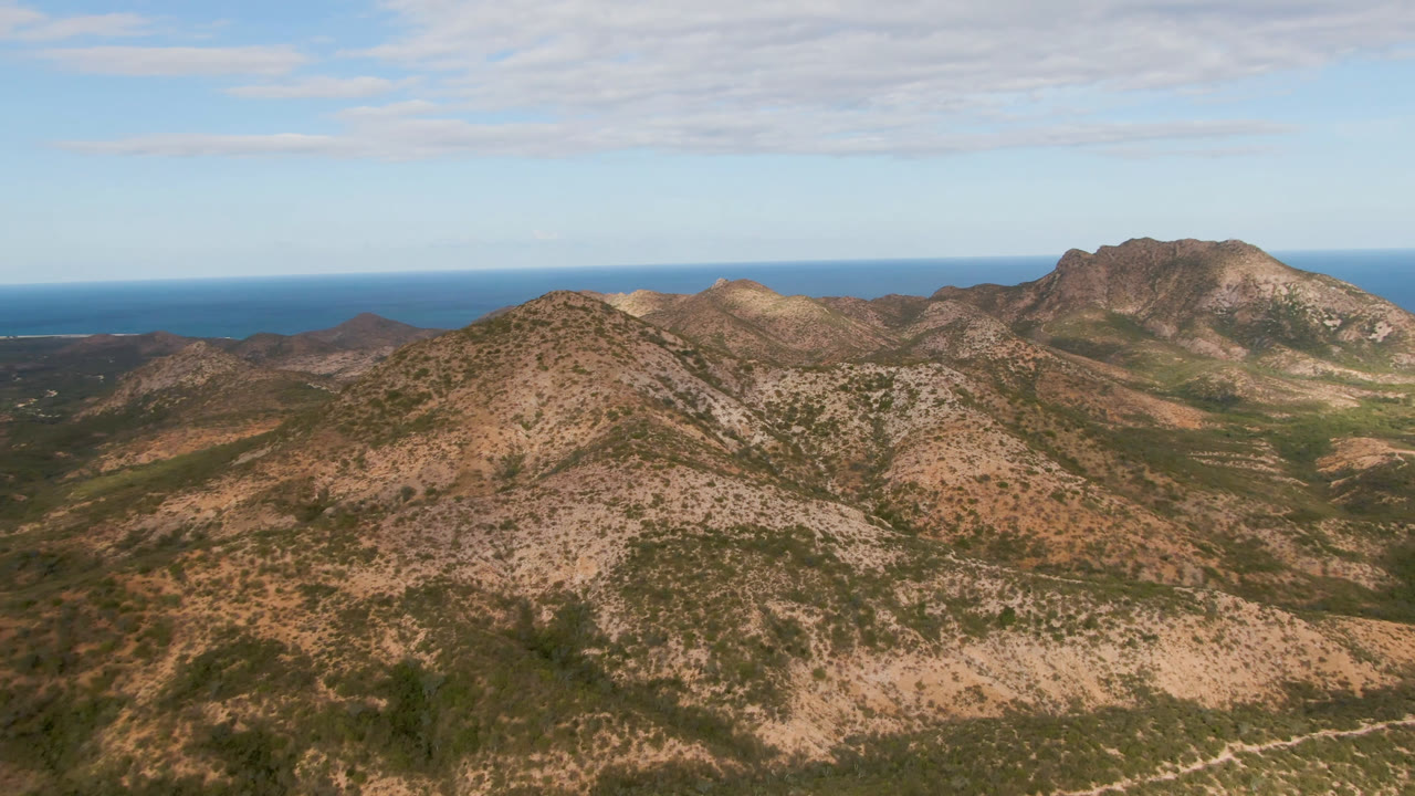 Cabo Pulmo mountain slopes fill the frame with scrub-covered ridges, a flat blue ocean band behind them, and no visible people.