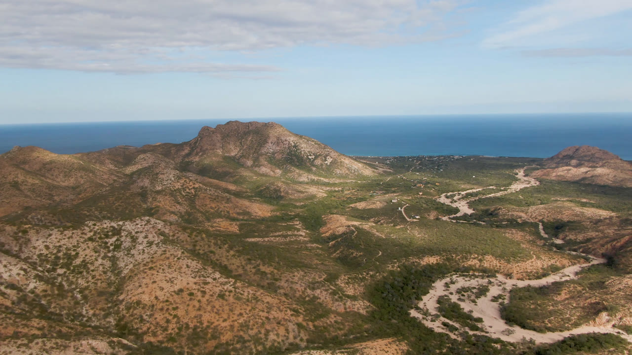 Aerial view of arid mountains, winding road, and ocean horizon.