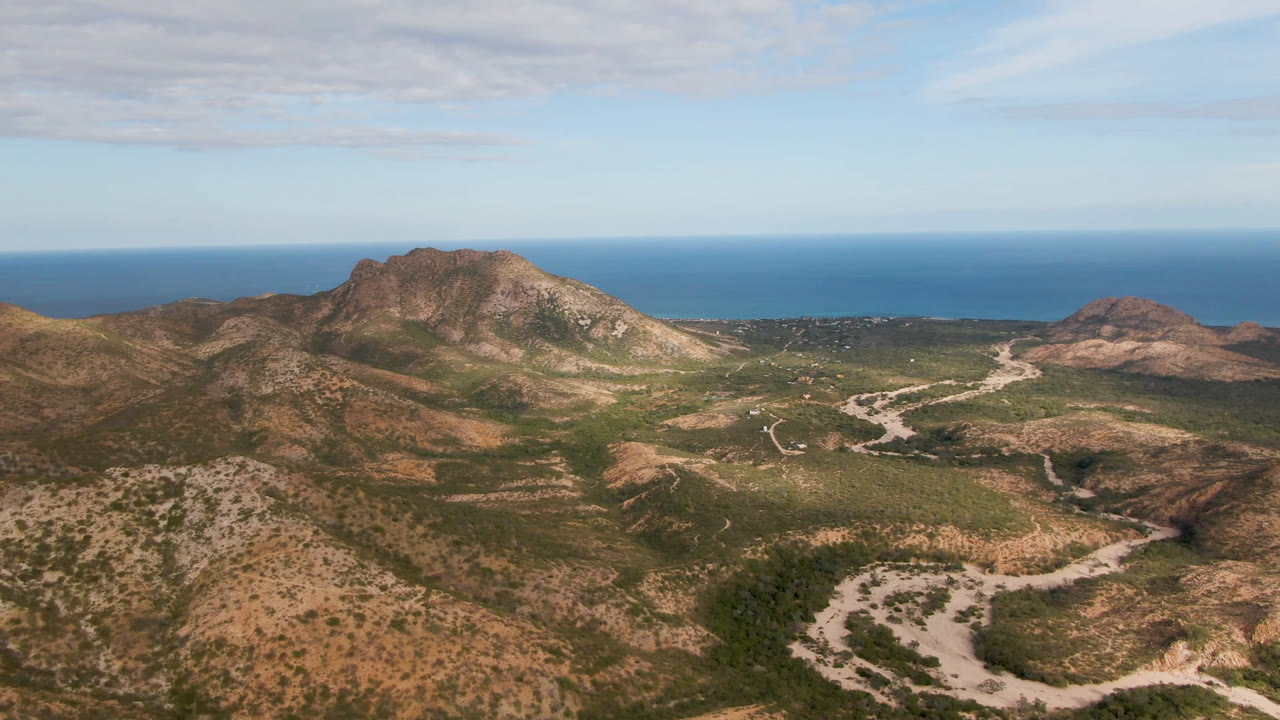 Aerial view in Cabo Pulmo showing the central rocky ridge, branching pale road lines, scrub-covered slopes, distant ocean, and no visible people.