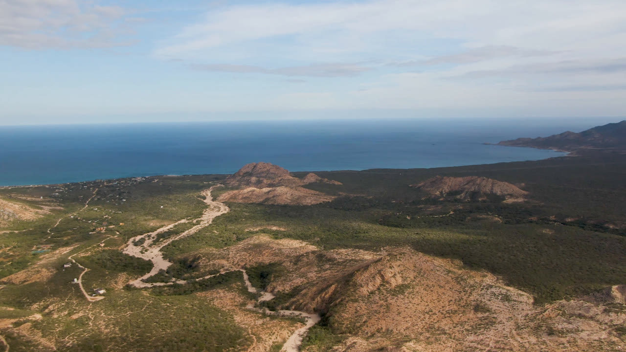 Aerial landscape with dry hills, branching dirt tracks, scrubland, and blue sea.