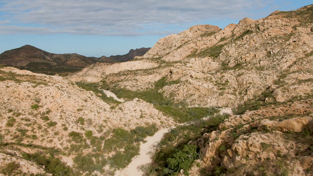 Desert mountain valley with rocks, scrub, and a pale trail or wash.