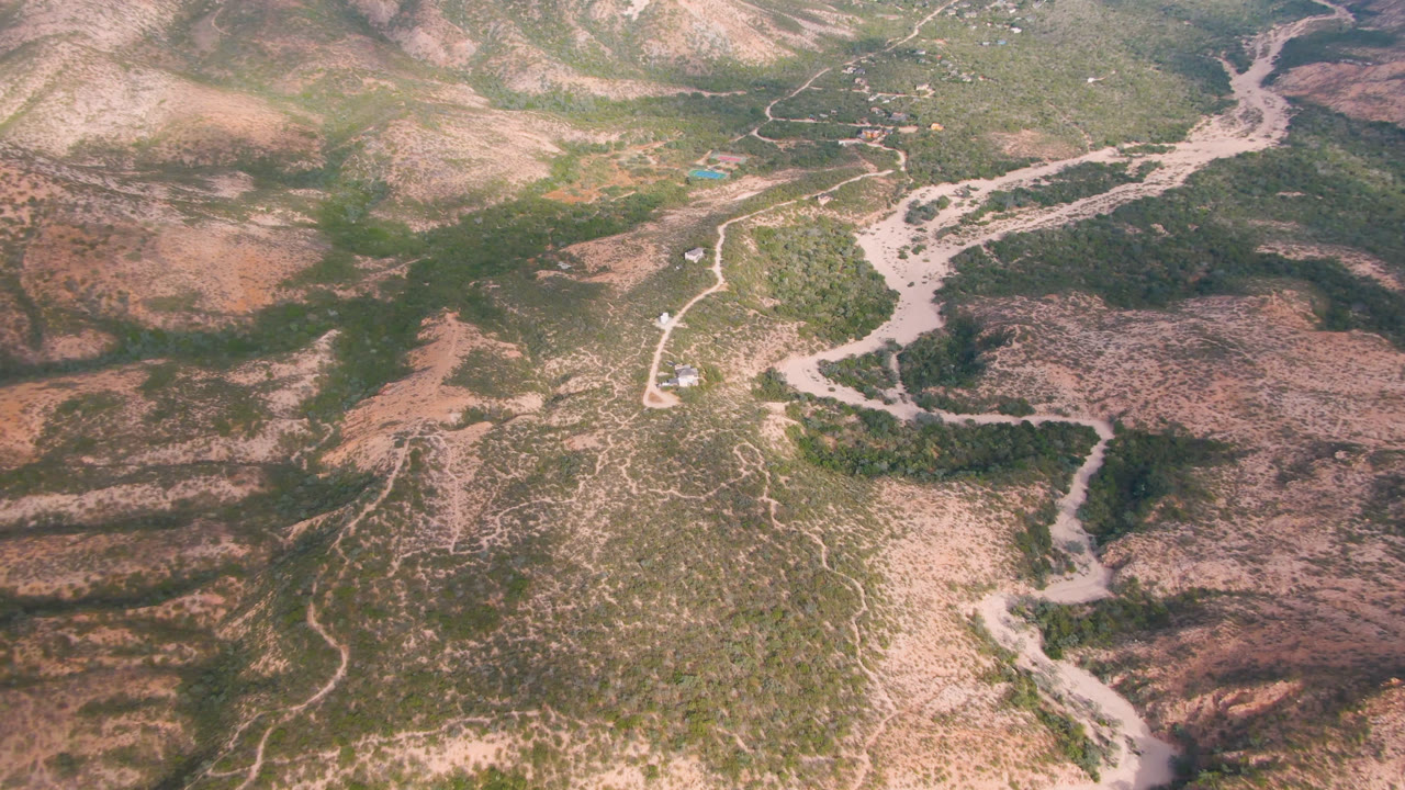 Oblique aerial view of scrub mountains, a pale wash, and a winding road.