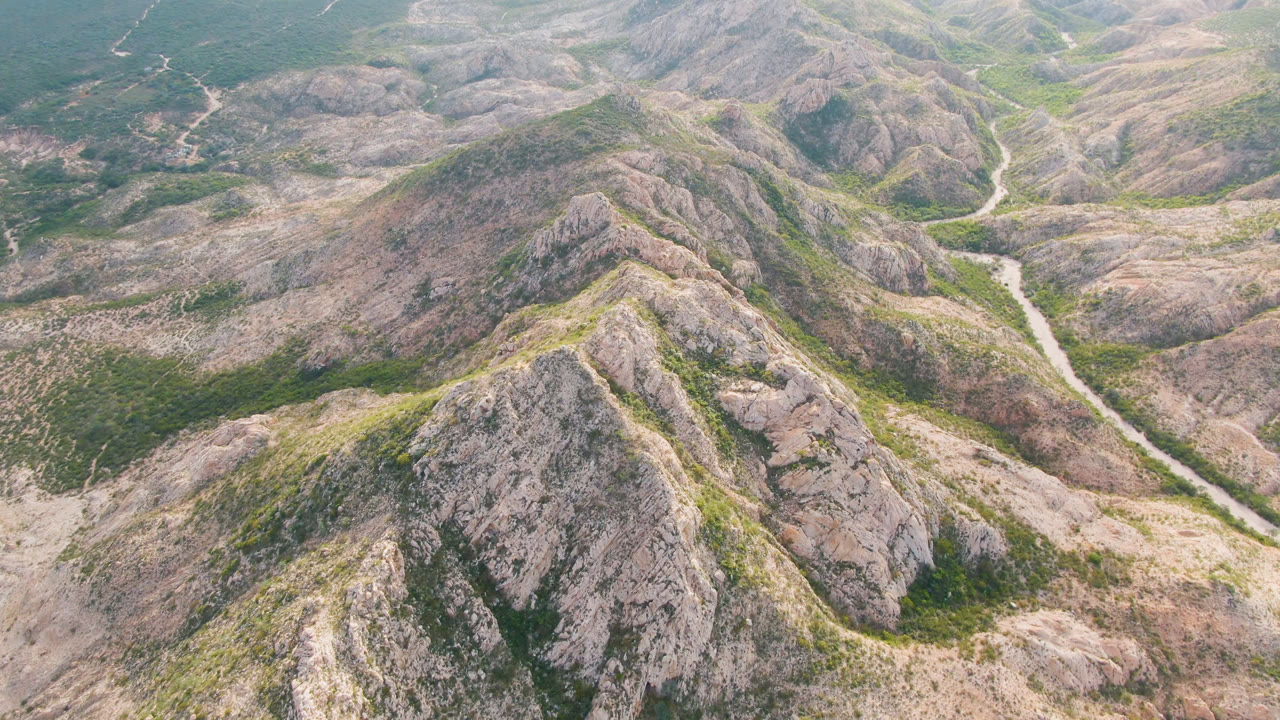 High aerial view over rocky hills in Cabo Pulmo, Baja California Sur, with a pale dirt road winding through the central valley and no visible people.