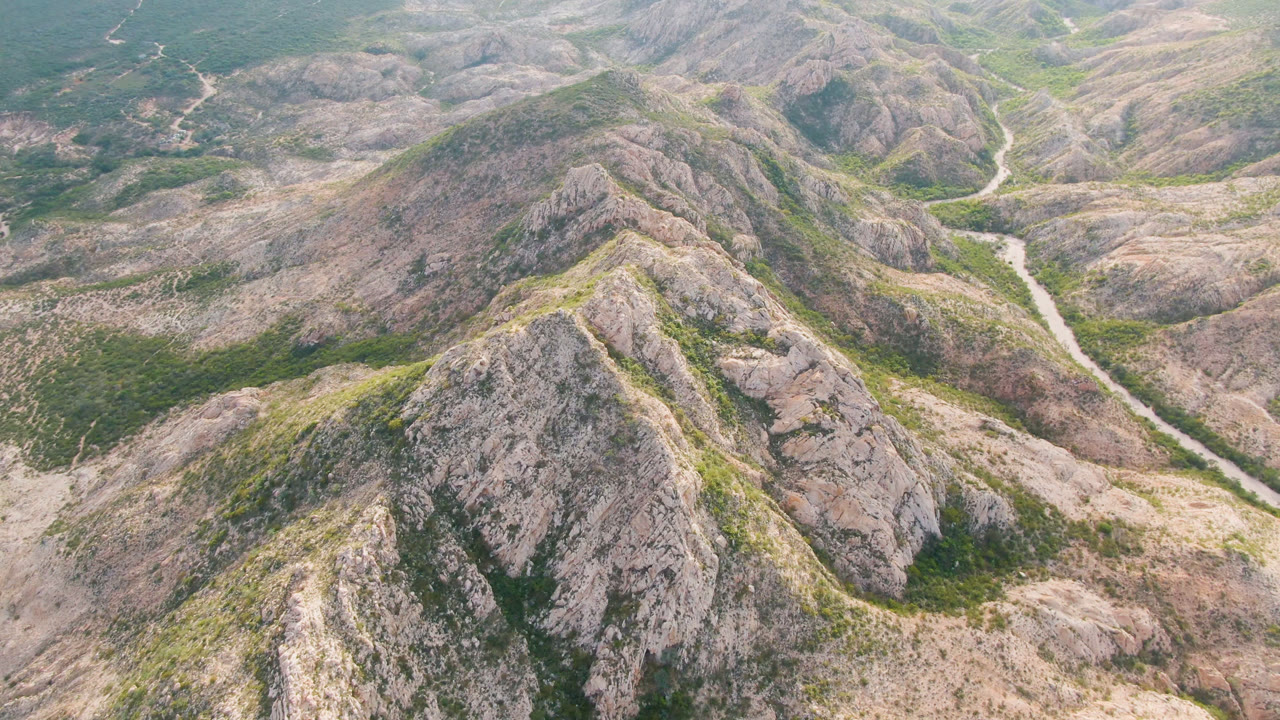 Opening frame of rocky hills in Cabo Pulmo, Baja California Sur, with a pale road cutting through the center valley and no visible people.