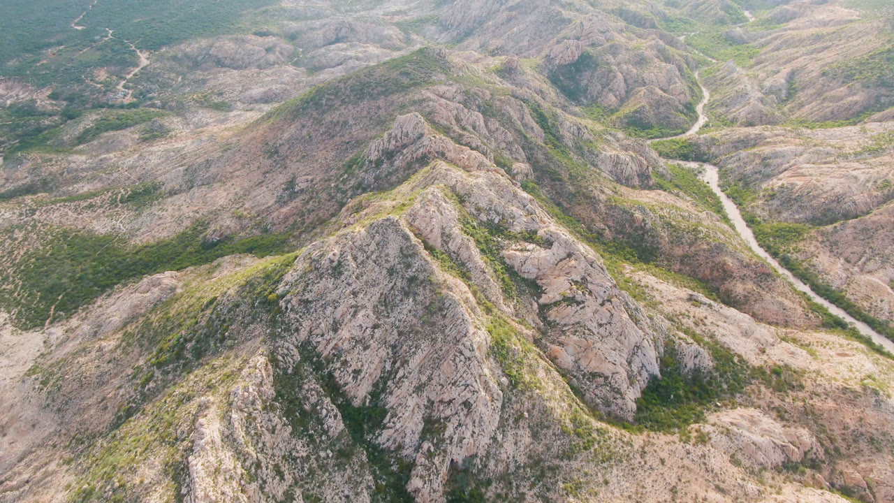 Second frame in Cabo Pulmo showing the main rocky ridge slightly closer in composition, with green scrub patches and no visible people.