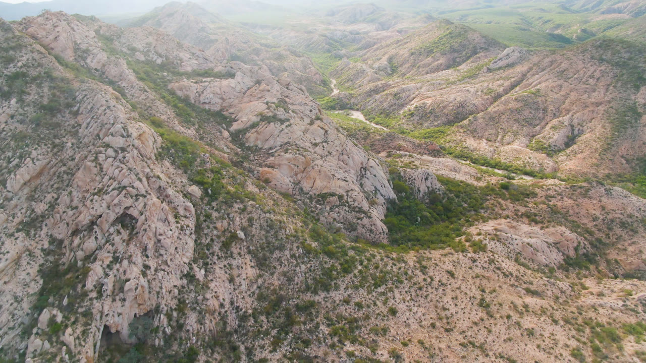 Drone perspective over jagged ridges and a scrub-filled valley.