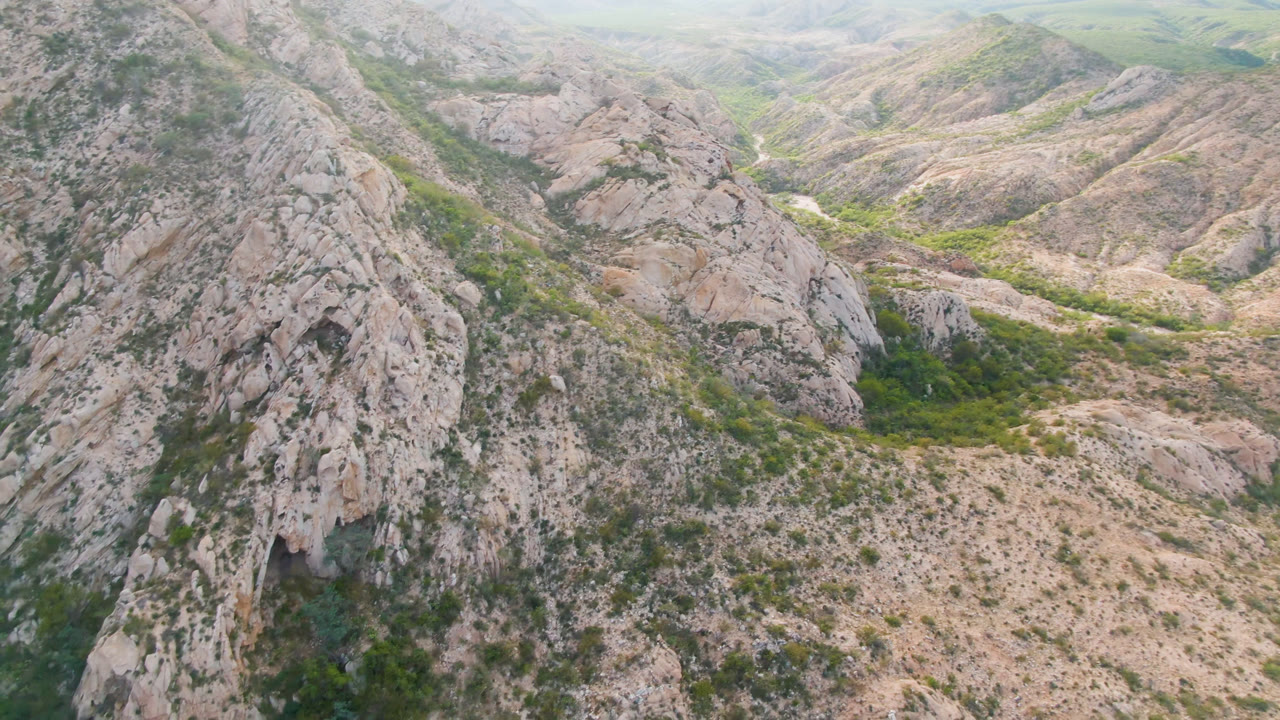 Opening frame of Cabo Pulmo mountain ridges with pale rock faces, scrub vegetation, hazy hills beyond, and no visible people.