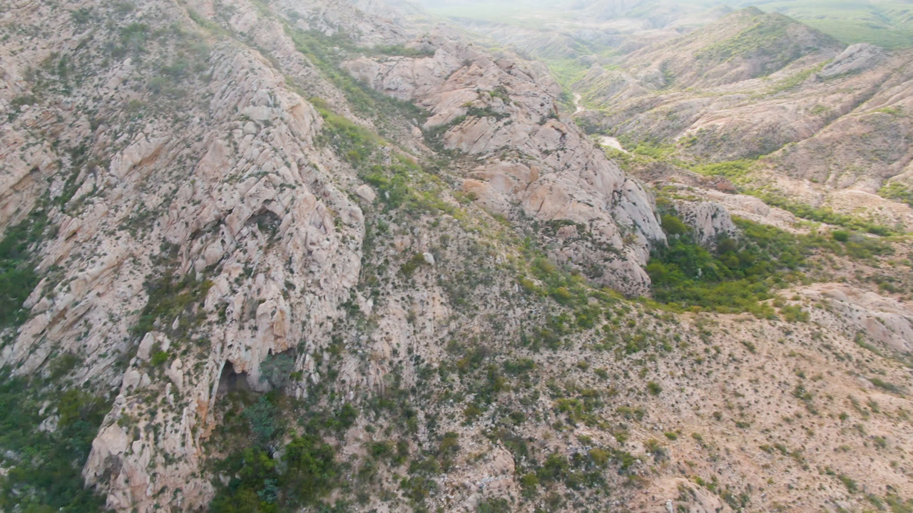 Second frame over Cabo Pulmo rocky slopes, with a darker green valley channel running through pale stone and no visible people.