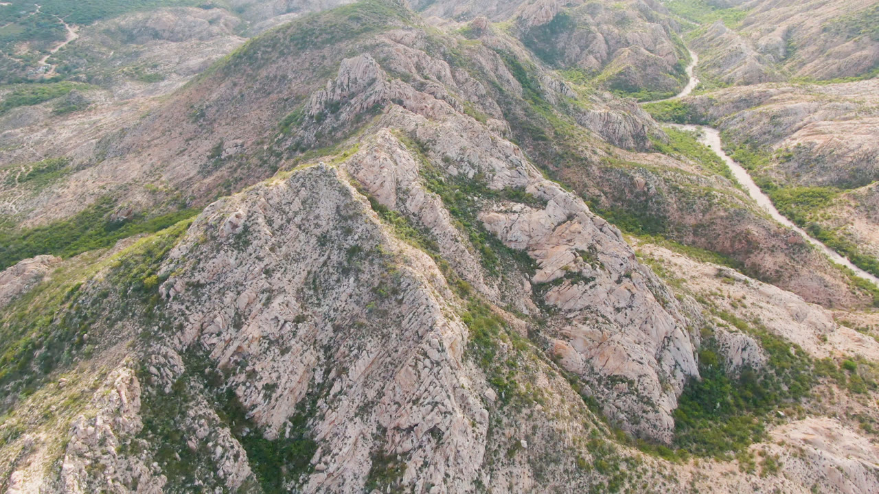 Aerial view in Cabo Pulmo showing the road more centered between ridged rock slopes, scattered green vegetation, and no visible people.