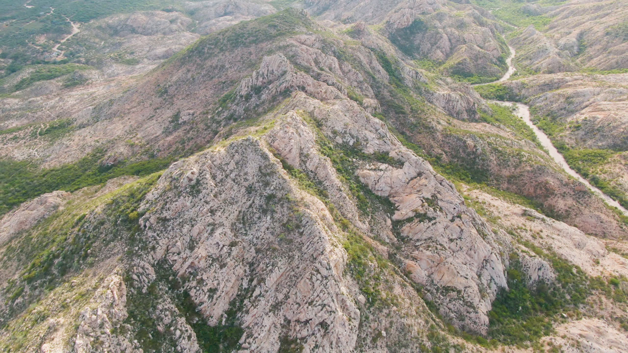 Aerial landscape of rugged hills with green gullies and a winding pale route.
