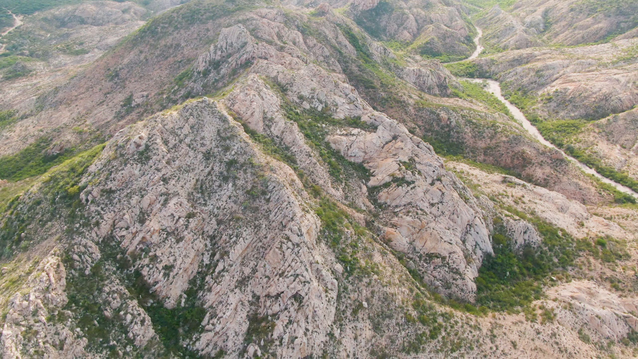 Aerial view of rocky hills with green gullies and a pale winding valley line.