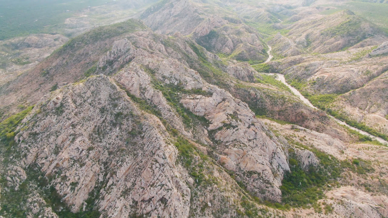Aerial frame from Cabo Pulmo, Baja California Sur, centered on a broad rocky ridge with the winding river valley visible behind it and no visible people.