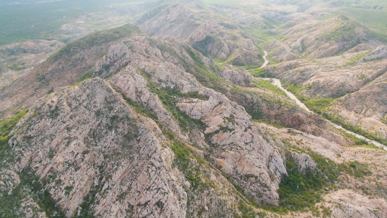 Drone-height view of dry ridges descending toward a vegetated river channel