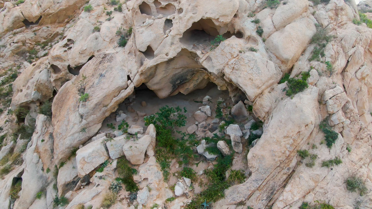 Overhead rocky mountain detail with cave holes, boulders, and green vegetation patches.