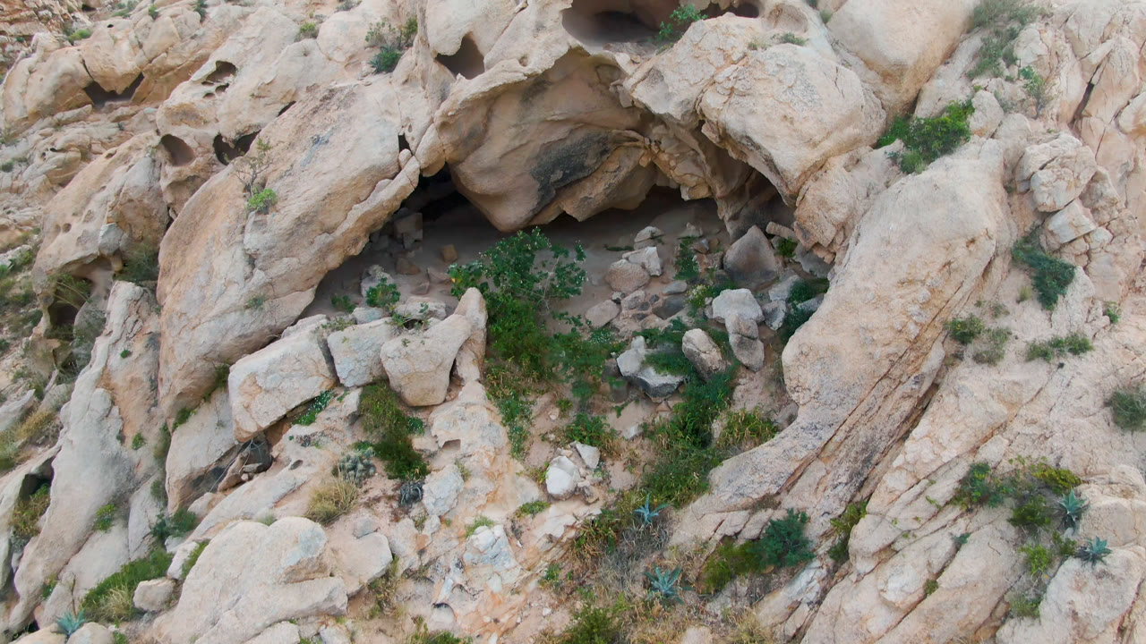 Top-down desert rock formation with cave shadow and scrub plants.
