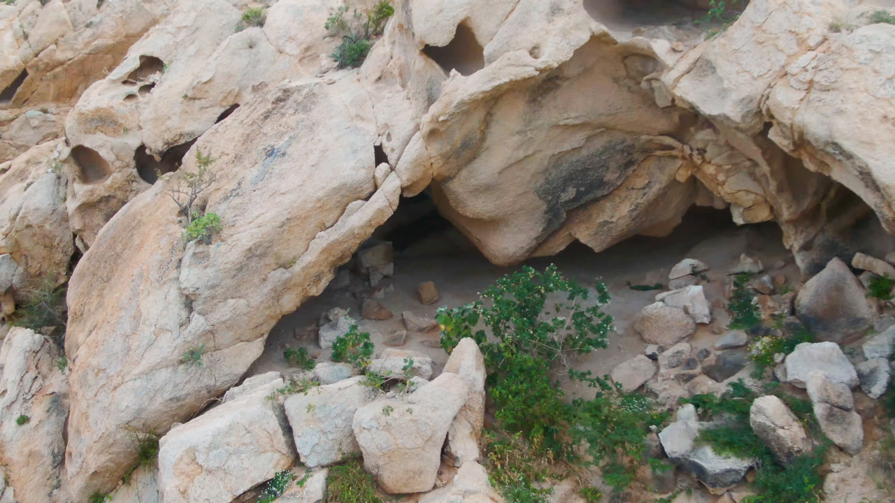 Rock alcove with pale boulders, brush, and sandy floor