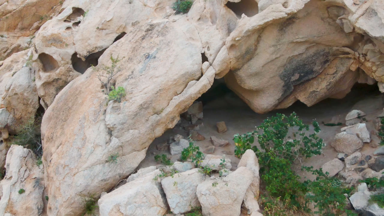 Aerial view in Cabo Pulmo, Baja California Sur with the rock face slightly shifted across frame, showing rounded holes, a shadowed recess, loose stones, and no visible people.