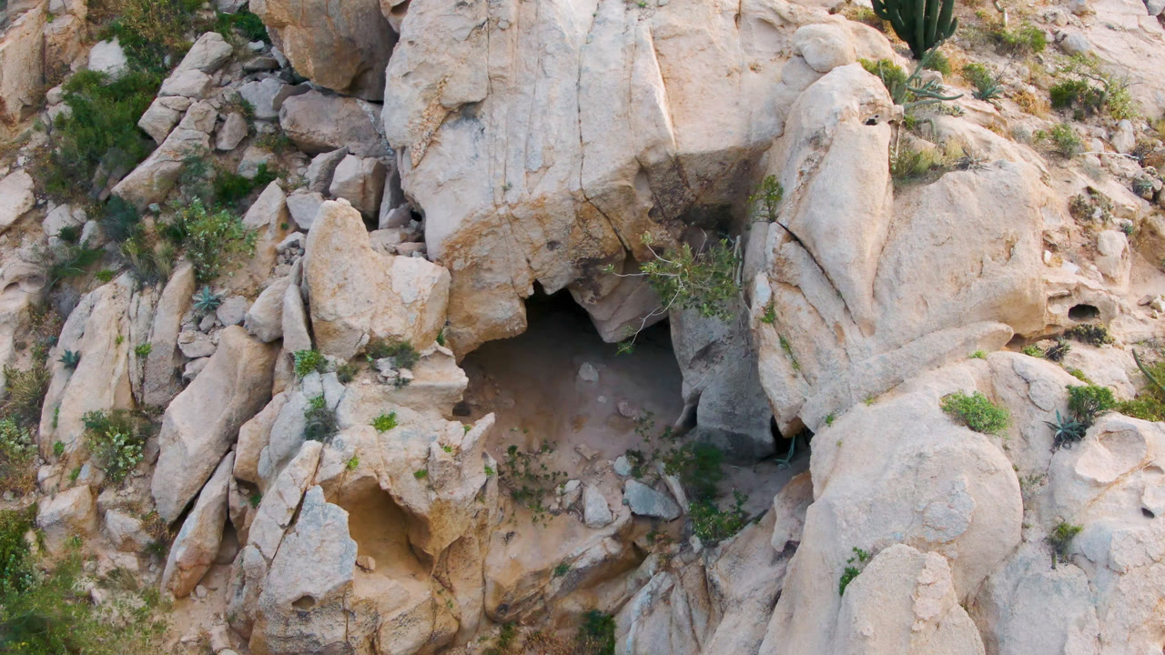 One second in, the Cabo Pulmo grotto sits below smooth tan boulders, with scattered green shrubs and no visible people.