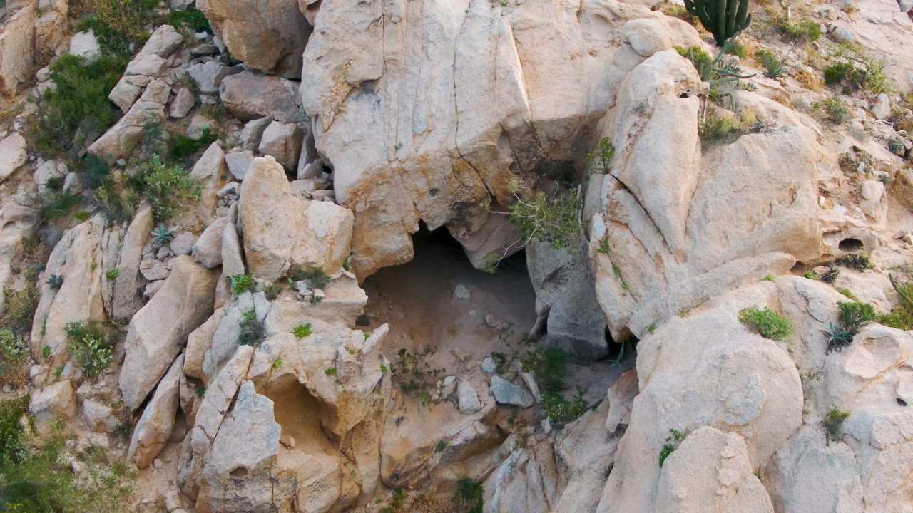 Dark cave recess surrounded by tan stone and hillside vegetation