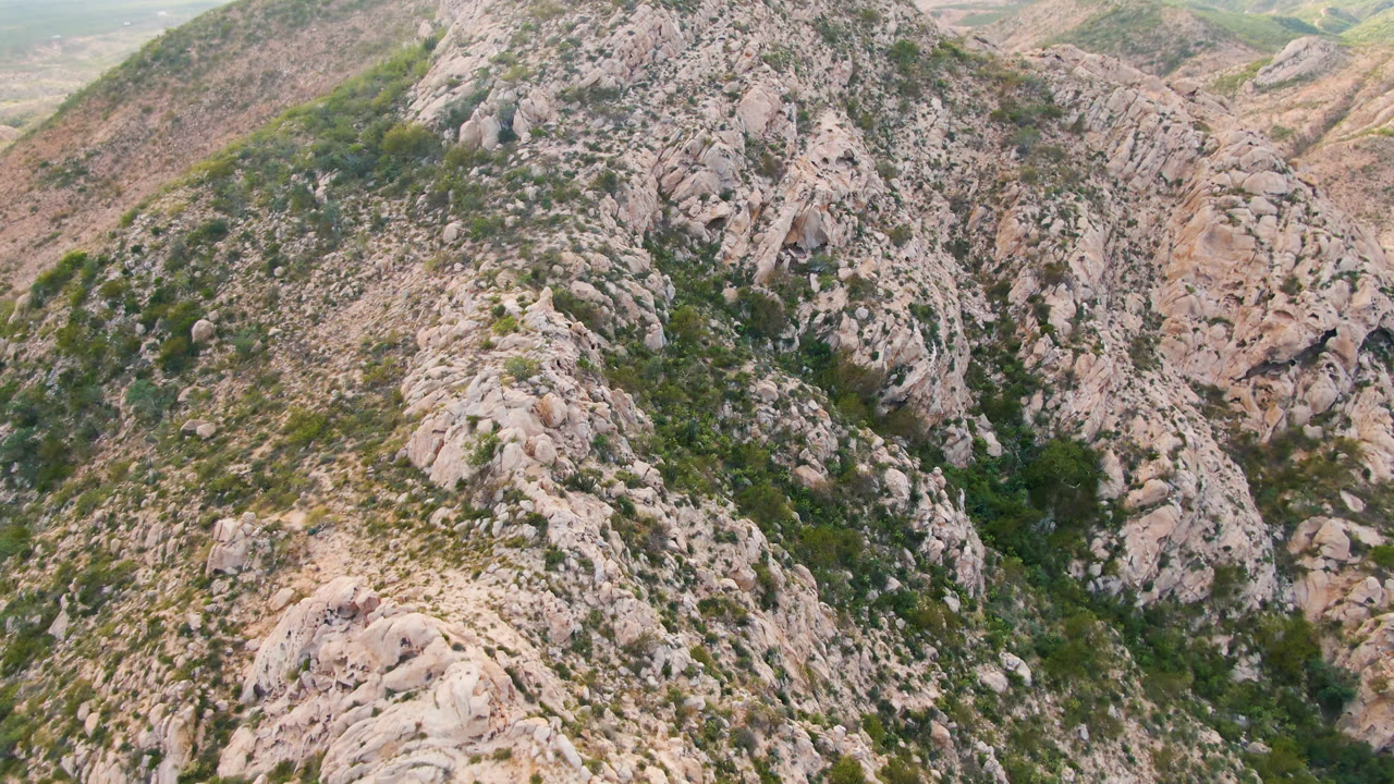 Aerial view in Cabo Pulmo, Baja California Sur, showing a pale rocky ridge dropping toward a dry valley with sparse shrubs and no visible people.