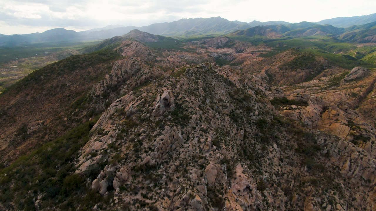 Cabo Pulmo aerial view with the main stony ridge centered, darker green vegetation on the near slope, pale rock cuts to the right, and no visible people.