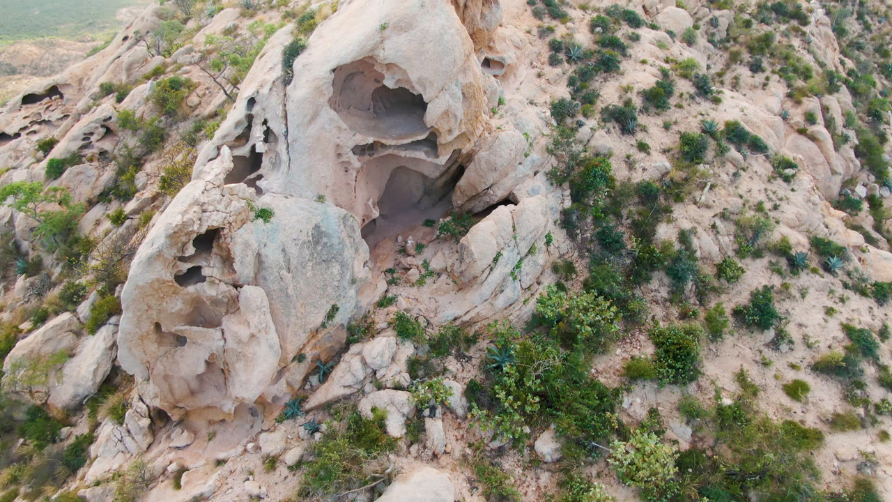 Aerial view of an eroded tan rock formation on a scrub-covered hillside.