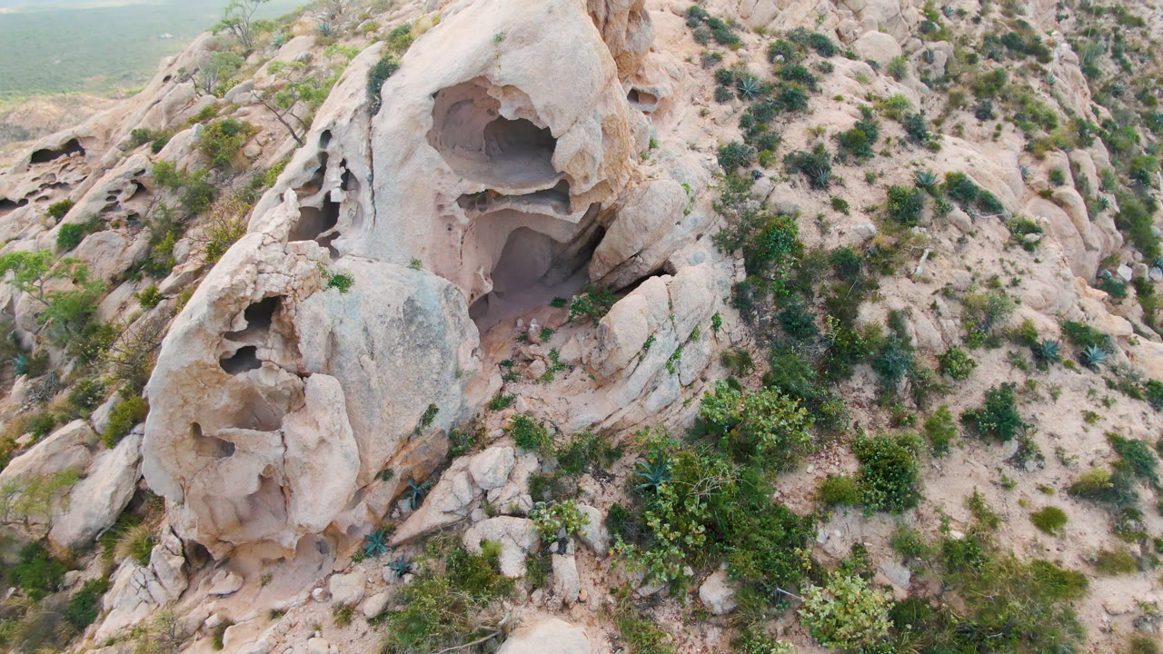 Aerial view in Cabo Pulmo showing the hollowed rock face slightly more centered, with scrub vegetation on the slope and no visible people.