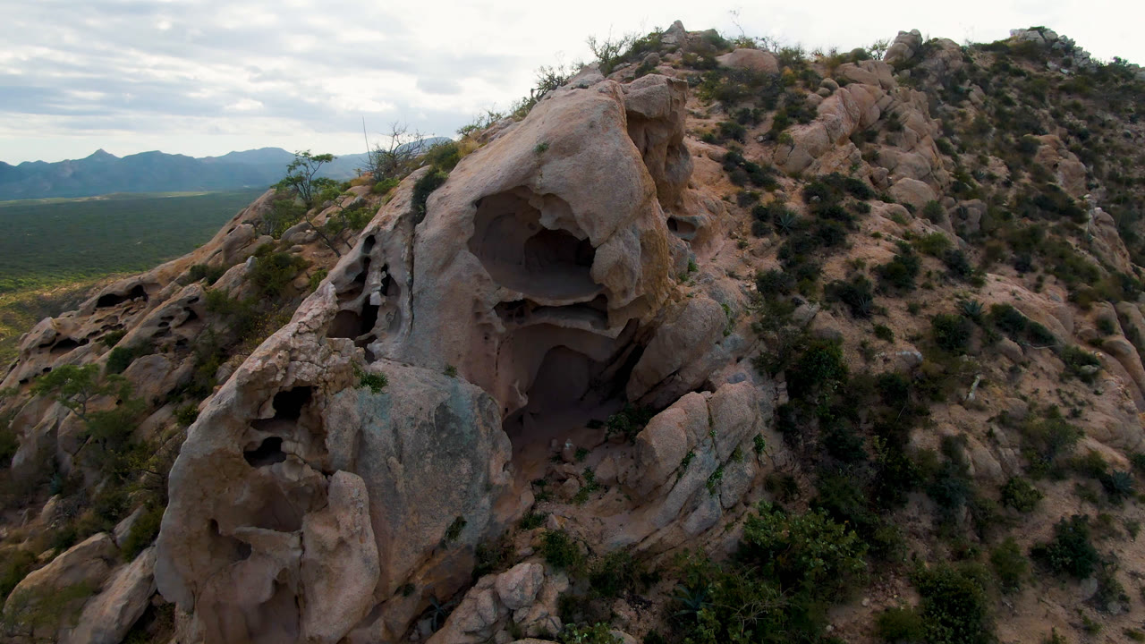 Weathered rock formation with hollow openings and desert mountains