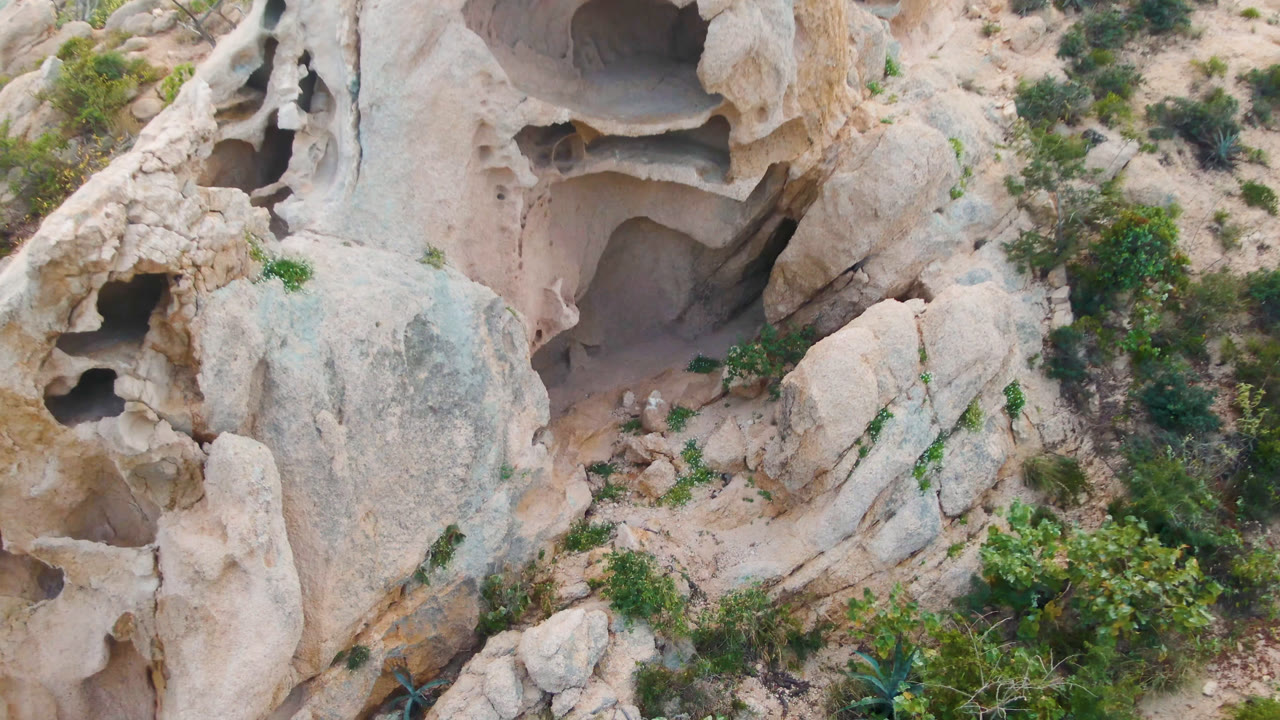 Second frame shows the Cabo Pulmo rock face from above, with one large dark recess, smaller holes, scrub plants, and no visible people.