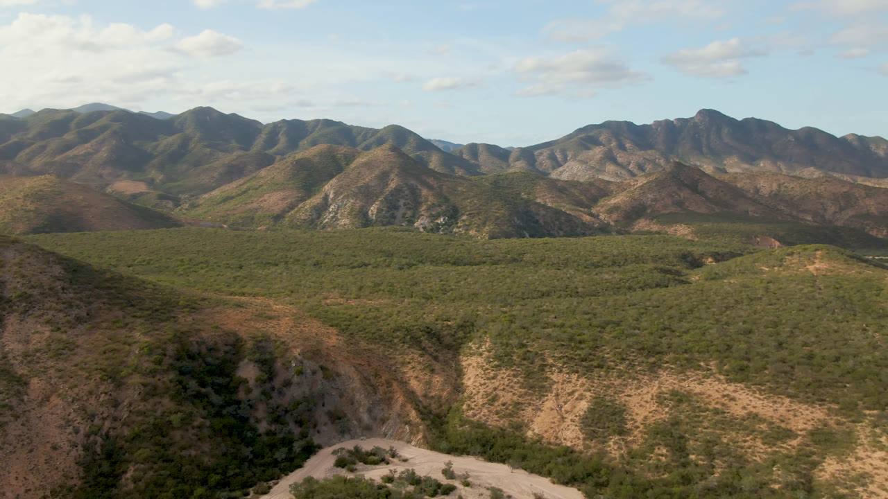 Aerial view of dry mountains and green valley vegetation under a blue sky.