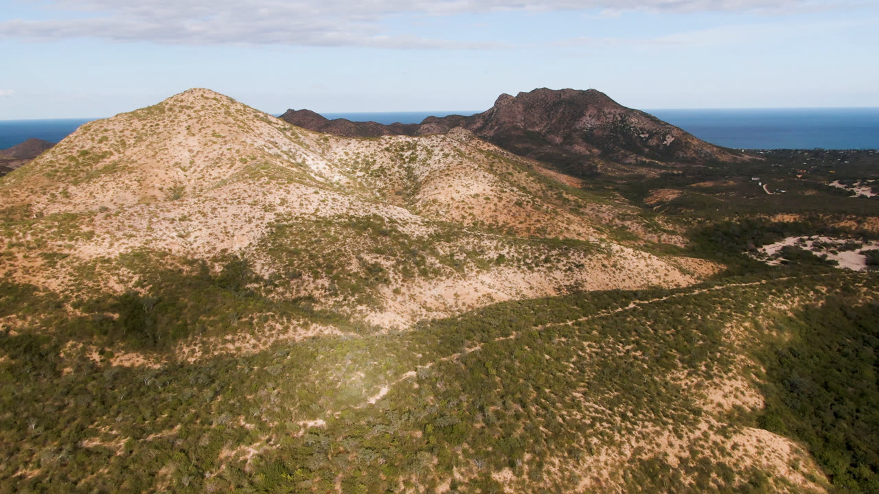 Opening frame of Cabo Pulmo, Baja California Sur mountains with a pale rocky slope in front, dark ridges behind, blue ocean on the horizon, and no visible people.