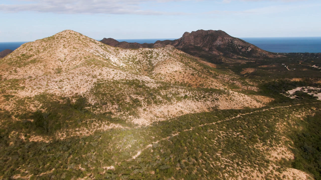 Wide aerial view of arid mountain ridges with ocean and sky in the background.