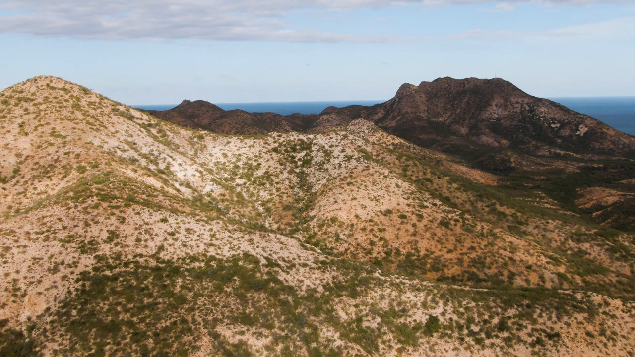 Arid mountain landscape with foreground hills, distant ridge, and ocean line.