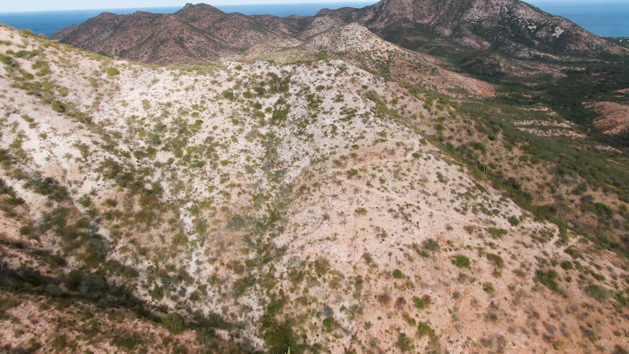 Drone view across dry hillside toward mountain range and ocean horizon