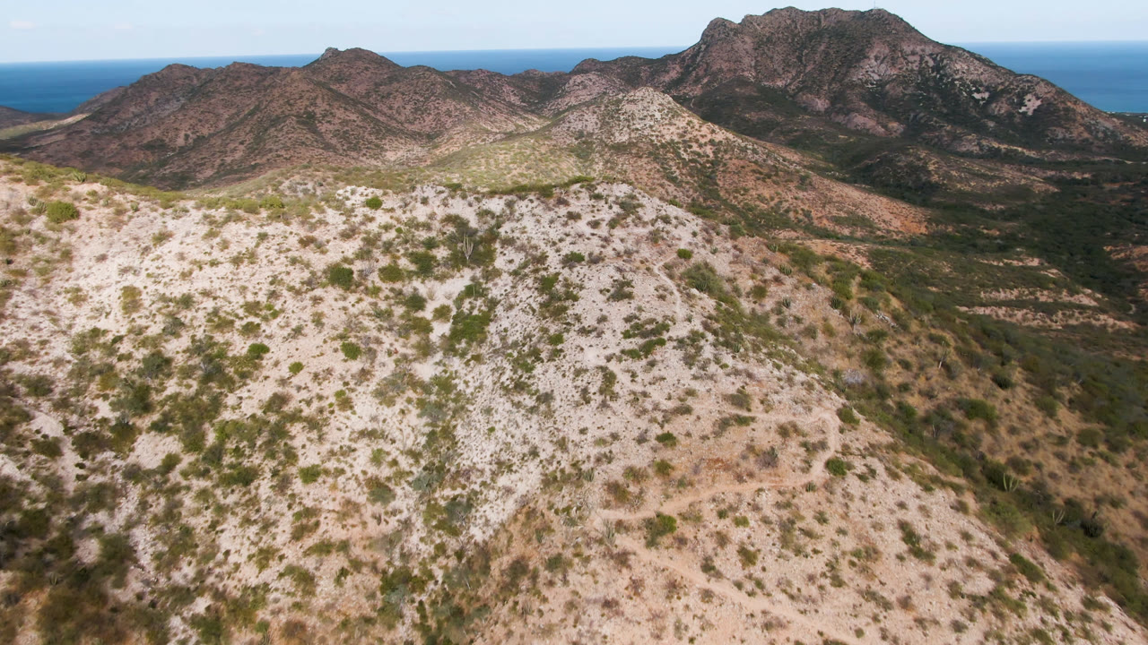 Drone-like aerial view across scrubby hills to a dark mountain peak and ocean.