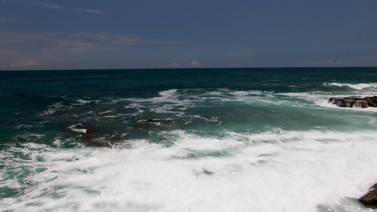 Wide ocean view with white surf breaking around dark rocks