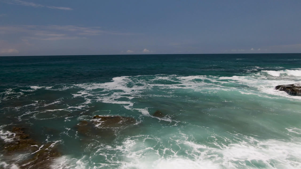 Laguna Beach ocean water shifts between deep green and turquoise as white foam trails around low rocks, with no visible people in the frame.
