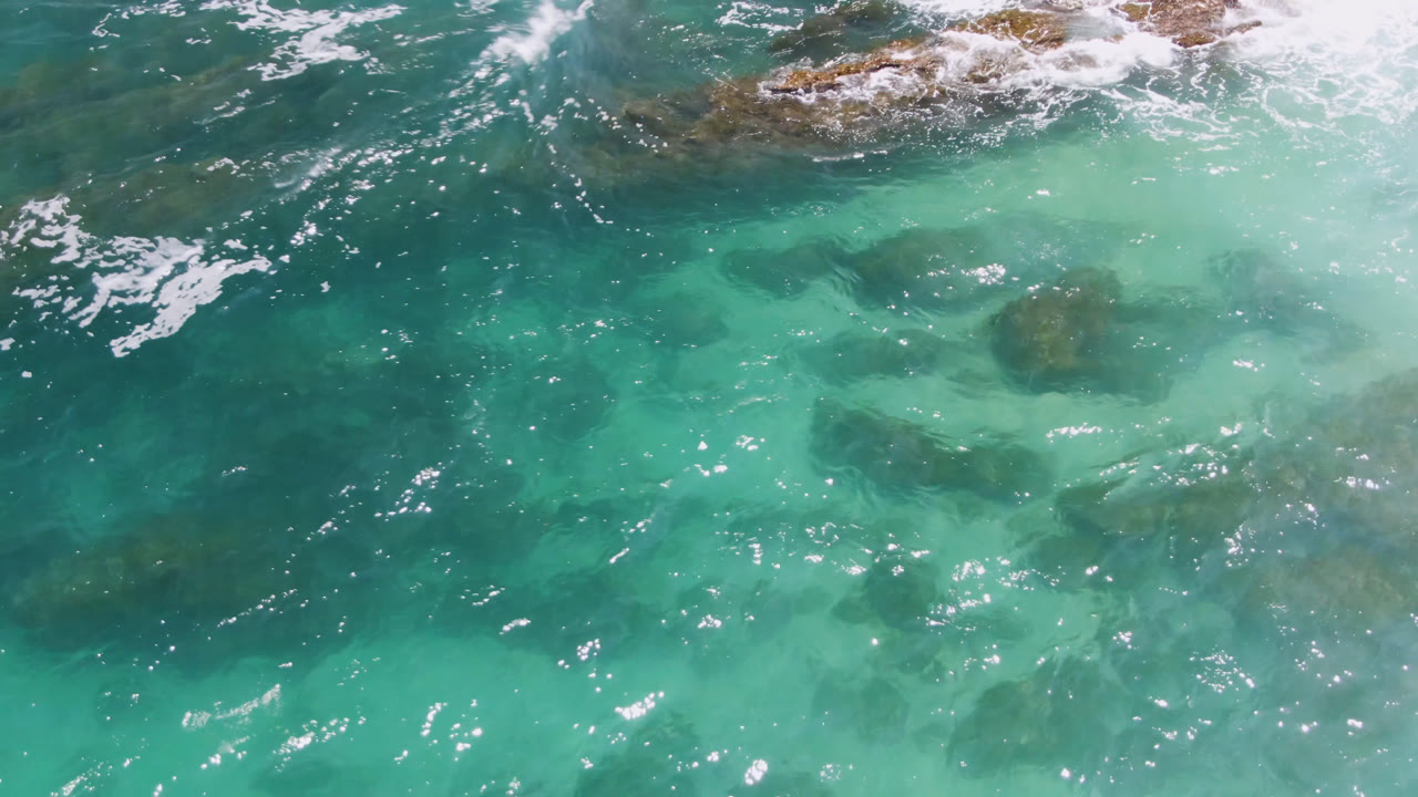 Bright turquoise sea with submerged reef shapes and surf breaking along the upper edge.