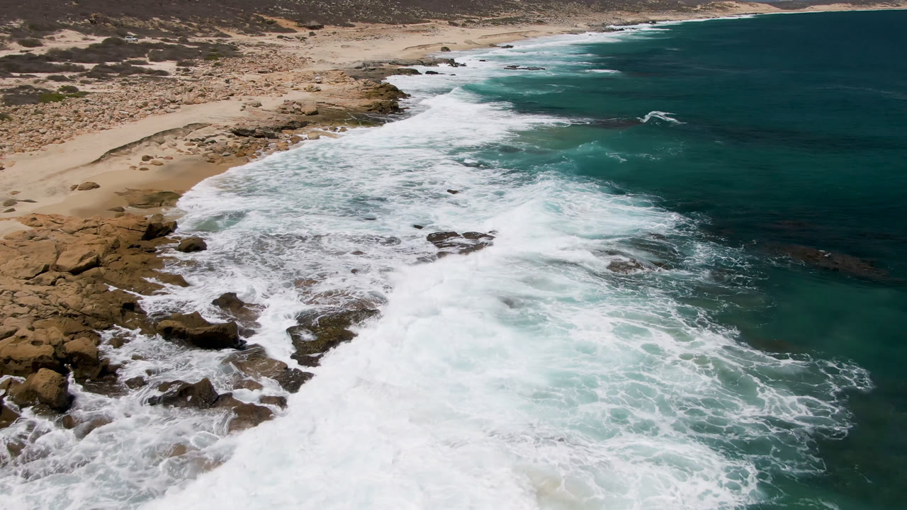 Large wave wash spreads across rocks and beach from above