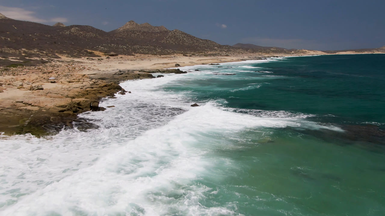 Ocean waves roll toward a rocky beach below dry mountains