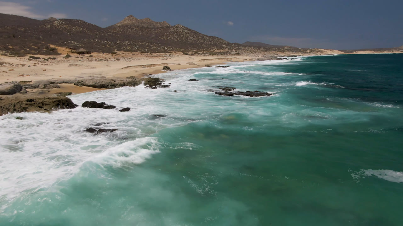 White surf crossing shallow turquoise water near rocks and beach