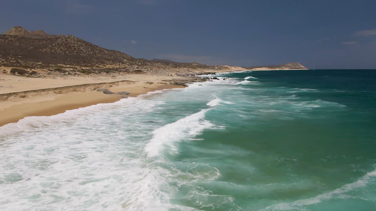 Wide coastal view with surf lines breaking along an empty sandy shore.