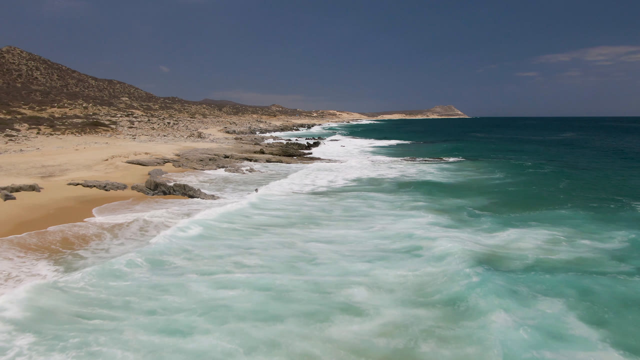 Aerial coastal view with surf, rocks, sand, and open ocean
