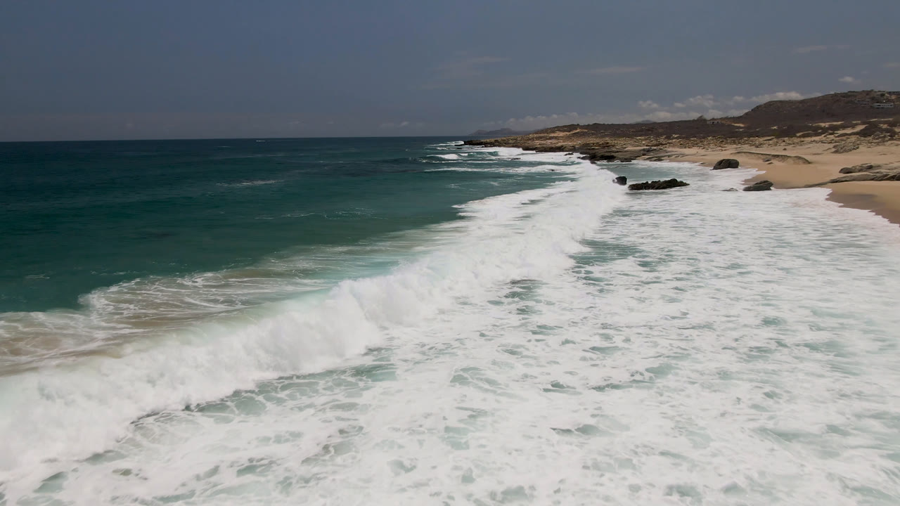 Aerial view of white surf rolling toward a sandy coast