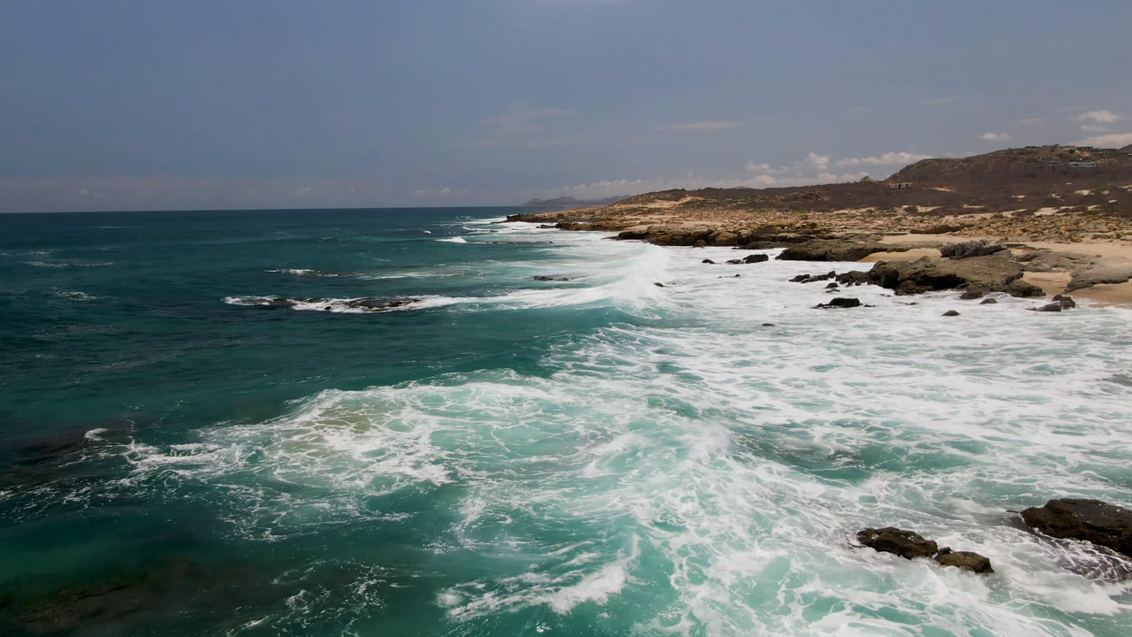 White waves push farther across the midground rocks at Laguna Beach, Baja California Sur, while open teal water fills the left side and no visible people appear.