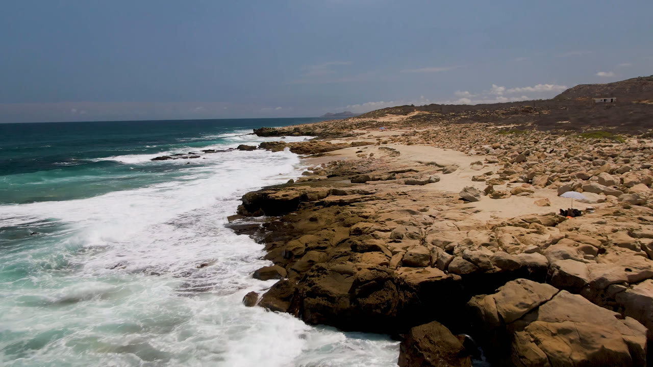 Coastal rocks and foamy waves under a clear sky.
