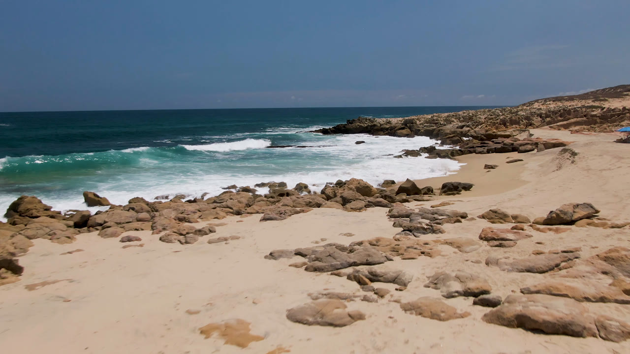 Rocky sandy beach with waves breaking under a blue sky.